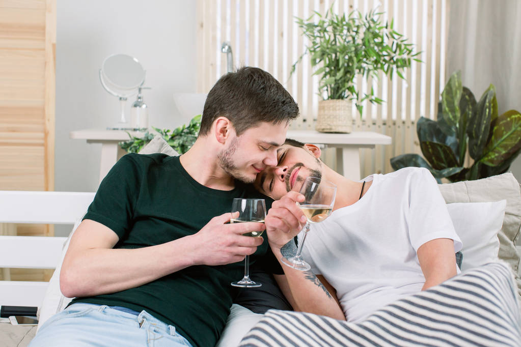 Europea feliz pareja gay bebiendo vino mientras se divierten en la cama, acariciando. Relaciones homosexuales y concepto alternativo de estilo de vida amoroso
 - Foto, imagen
