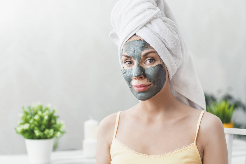 Gesichtspflege. attraktive junge Frau in Badetuch gehüllt, mit Lehmmaske im Gesicht. Hautpflegekonzept. Mädchen kümmert sich um Teint. Schönheitsbehandlungen - Foto, Bild