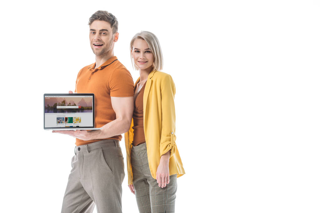 dobře vypadající usměvavý muž držící přenosný počítač na obrazovce, zatímco stojíte poblíž krásné ženy izolované na bílém - Fotografie, Obrázek