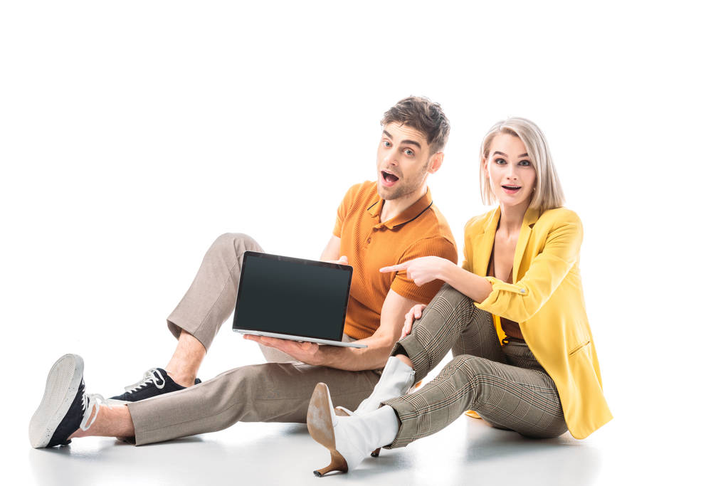 opgewonden man houden laptop met blanco scherm terwijl zittend in de buurt van mooie vrouw wijzend met de vinger op wit - Foto, afbeelding