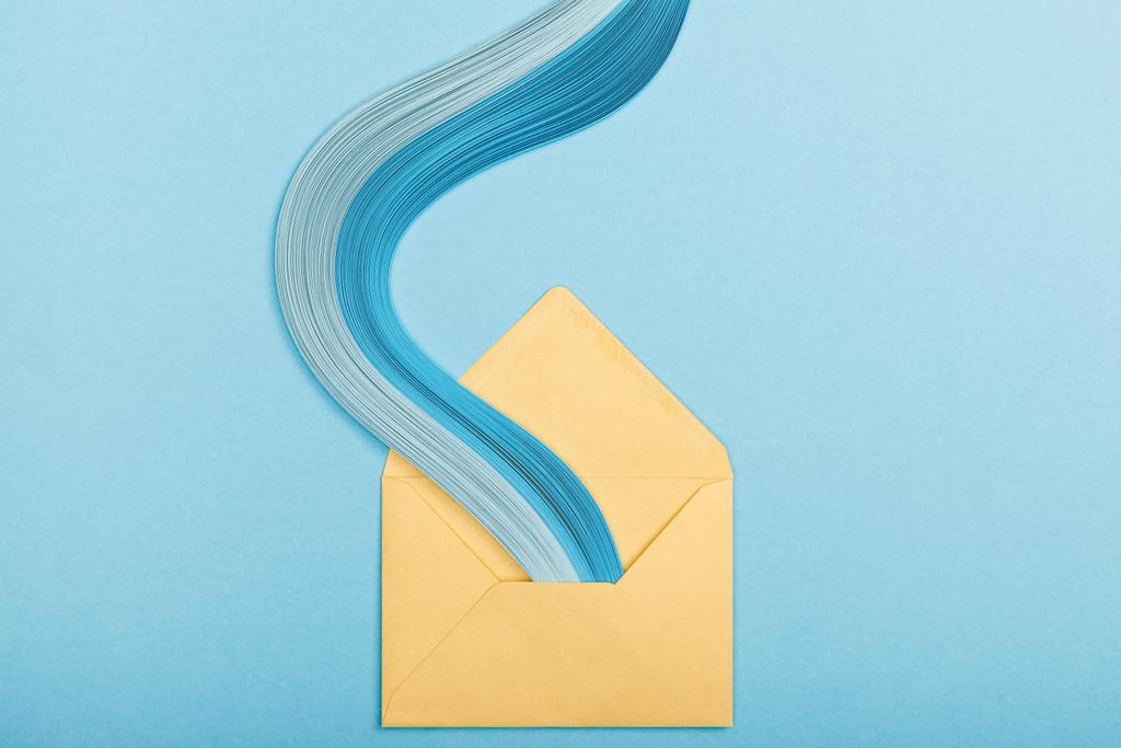 κάτοψη του μπλε καμπύλο αφηρημένη χαρτί γραμμές και κίτρινος φάκελος σε μπλε φόντο - Φωτογραφία, εικόνα