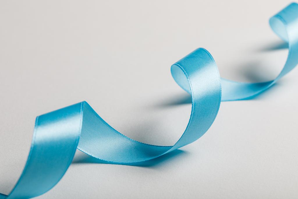 κοντινό πλάνο καμπυλωτή μπλε σατέν κορδέλα με γκρι φόντο - Φωτογραφία, εικόνα