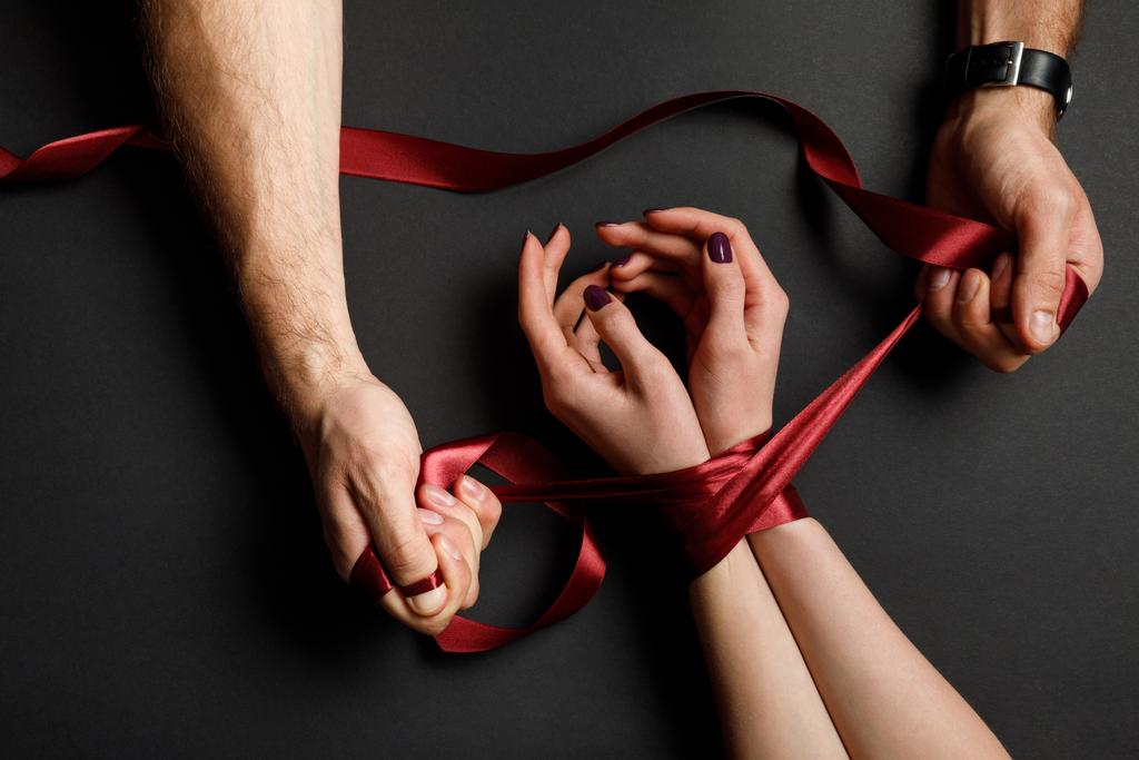 黒の背景に女性の手に赤いサテンのリボンを結ぶ人間観をトリミング - 写真・画像