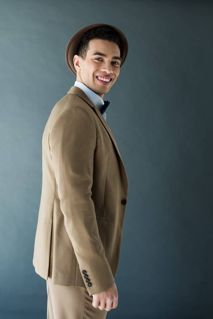 stylischer Mischlingsmann im Anzug, der in die Kamera schaut und isoliert auf grau lächelt - Foto, Bild