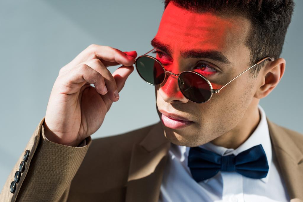 Stylowy mężczyzna rasy mieszanej w garniturze i okulary stwarzające na szaro z czerwonym światłem - Zdjęcie, obraz
