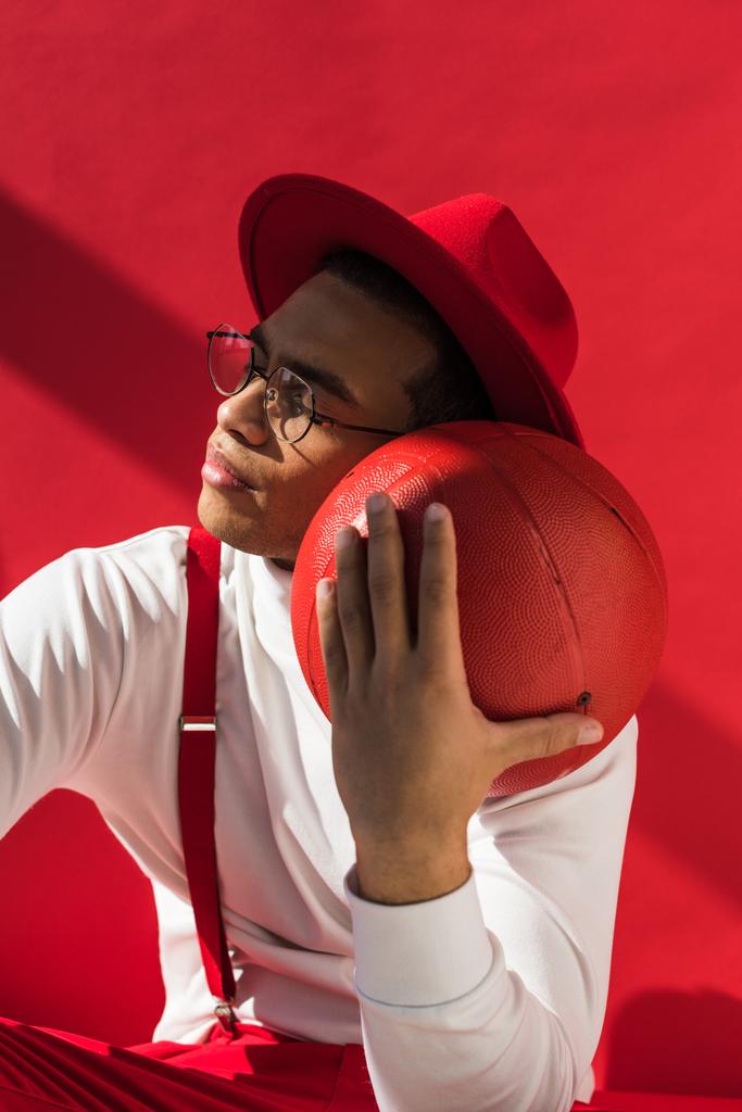 élégant homme mixte de race dans le chapeau et les bretelles posant avec le basket sur rouge
 - Photo, image
