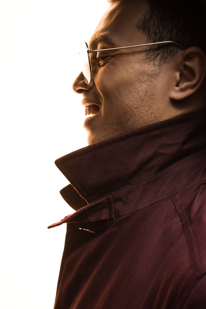 vista lateral del hombre de raza mixta en gafas de sol y abrigo sonriente aislado en blanco
 - Foto, imagen