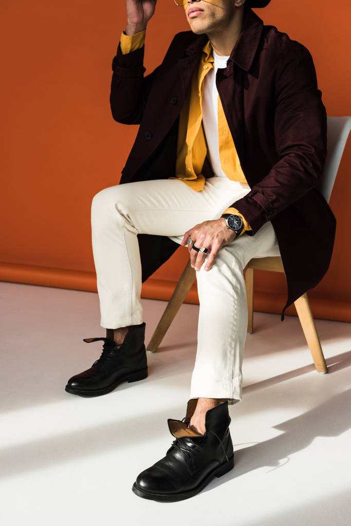 bijgesneden weergave van stijlvolle mixed race man zittend en poseren op Orange - Foto, afbeelding