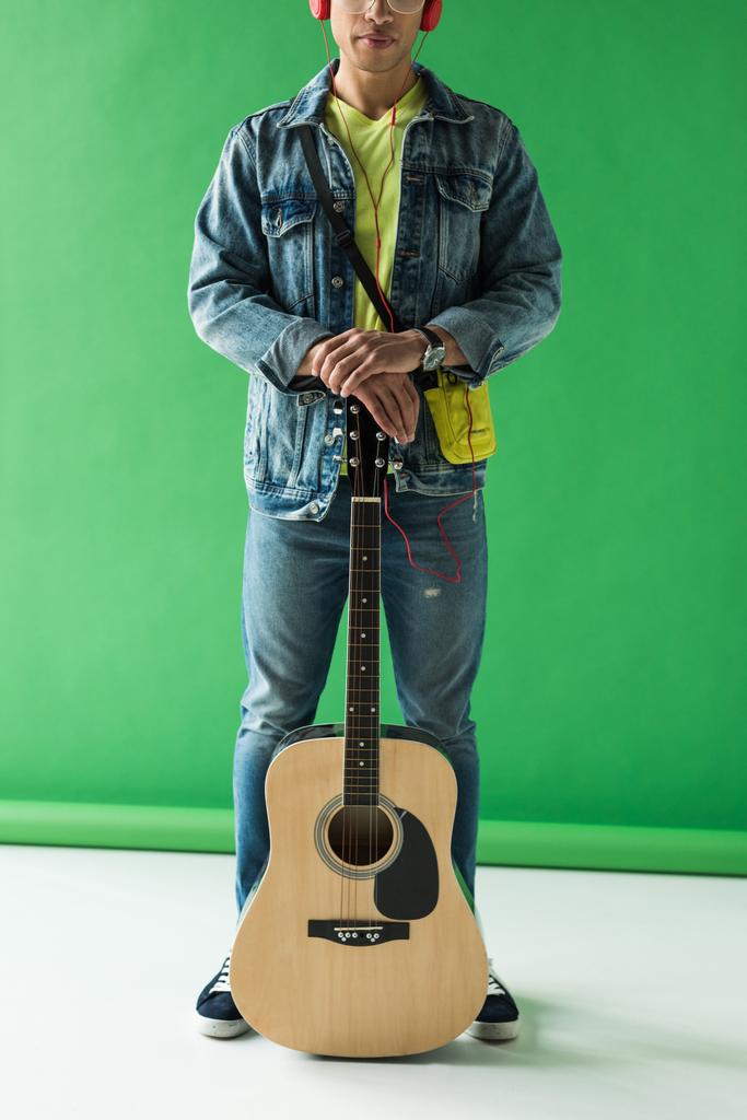 bijgesneden weergave van mixed race man in denim poseren met akoestische gitaar op groen - Foto, afbeelding