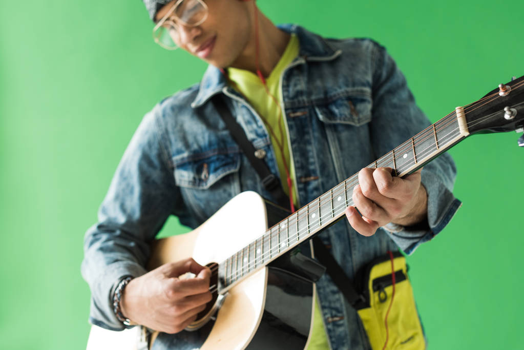 selectieve focus van mixed race man in denim spelen akoestische gitaar op groen scherm - Foto, afbeelding