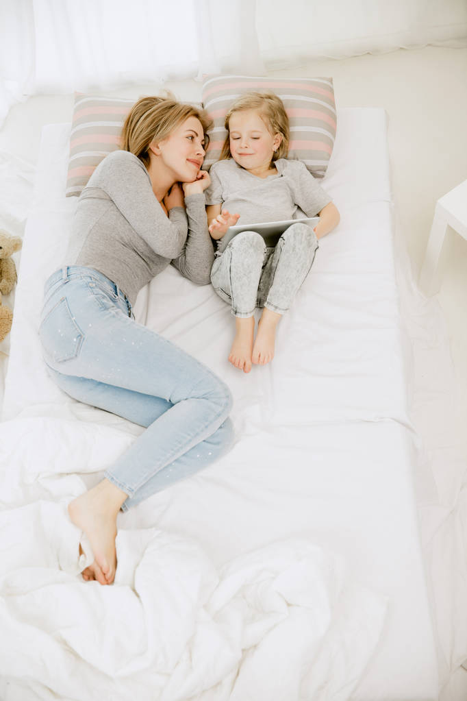 Joven madre y su hijita abrazándose y besándose en la cama
 - Foto, Imagen