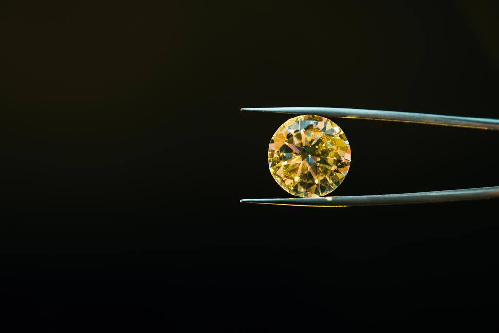 разноцветный желтый сверкающий бриллиант в пинцетах, изолированных на черном
 - Фото, изображение