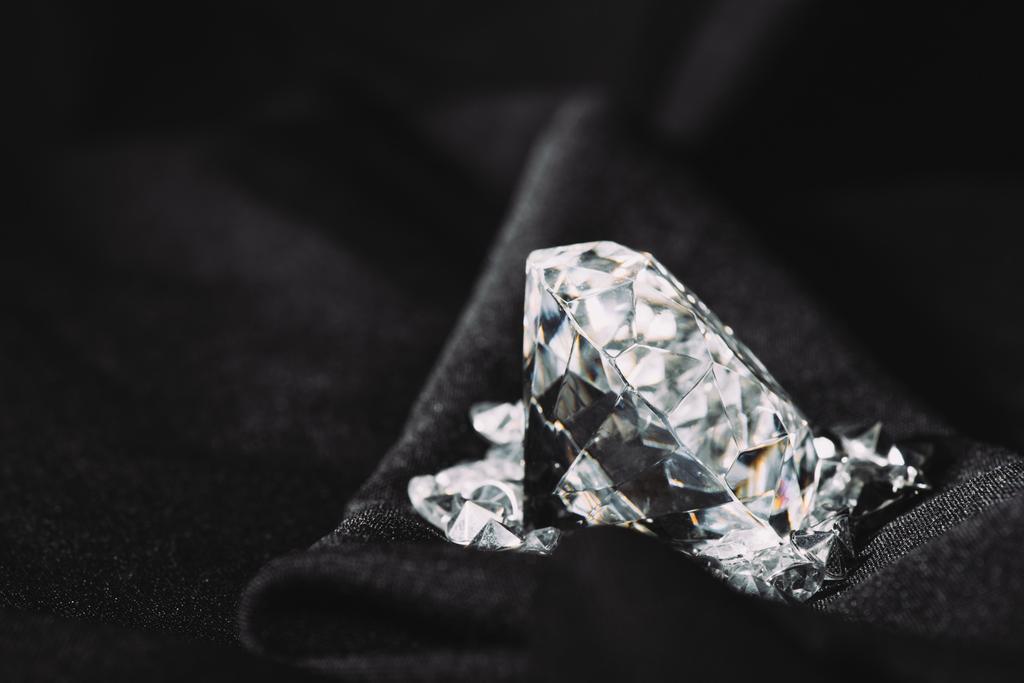 сверкающий чистый большой алмаз среди мелких на черной текстуре блестящей ткани
  - Фото, изображение