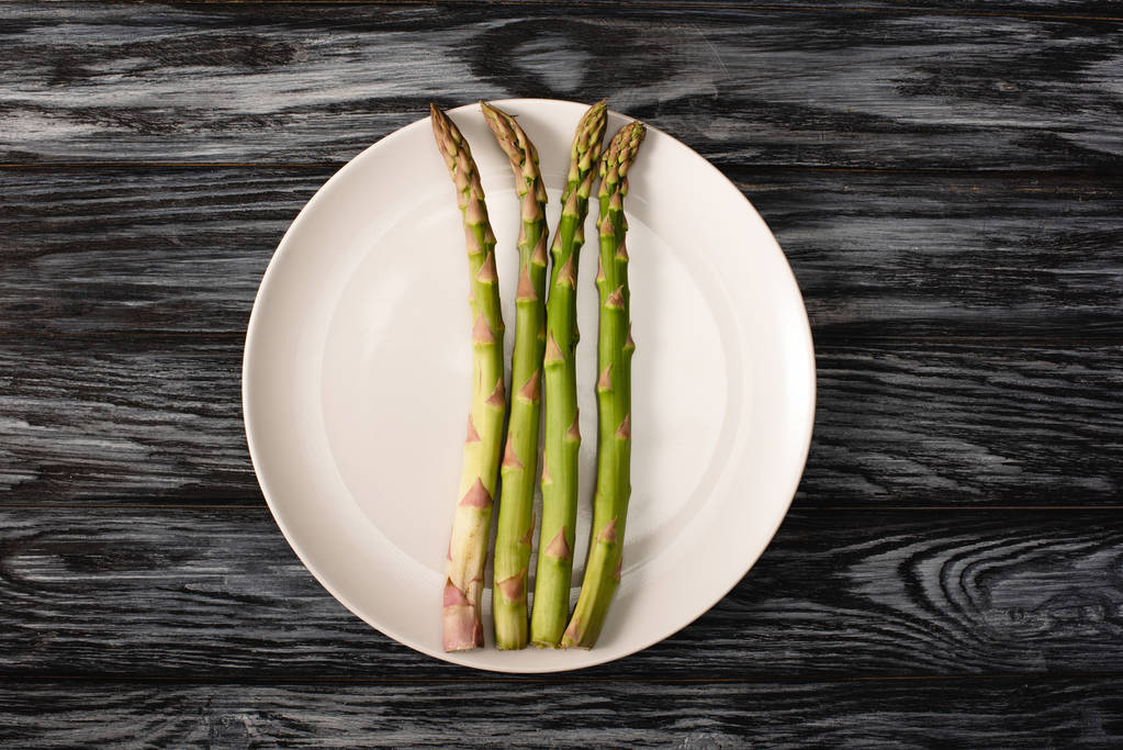 top view of organic asparagus on plate on grey wooden background - Photo, Image