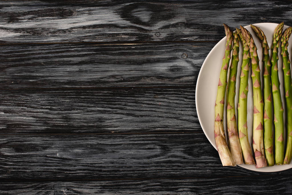 top view of green organic asparagus on plate on wooden background with copy space - Photo, Image