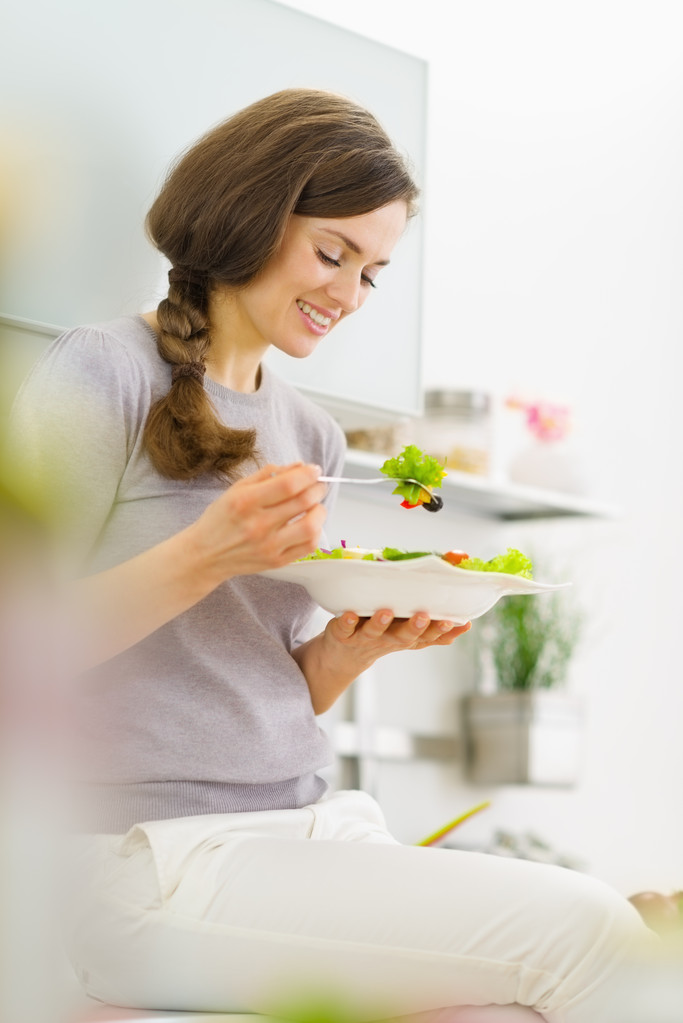 Jeune femme manger de la salade fraîche dans la cuisine moderne - Photo, image
