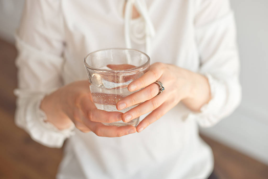 Γυναικεία χέρια που κρατούν μια σαφή ποτήρι νερό. Ένα ποτήρι καθαρό μεταλλικό νερό στα χέρια, υγιεινό ποτό - Φωτογραφία, εικόνα