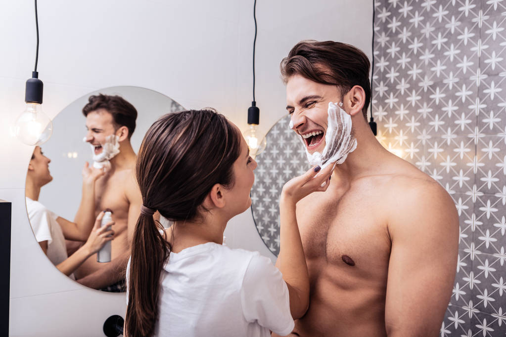 Муж смеётся, когда его жена наносит ему на лицо пену для бритья.
 - Фото, изображение
