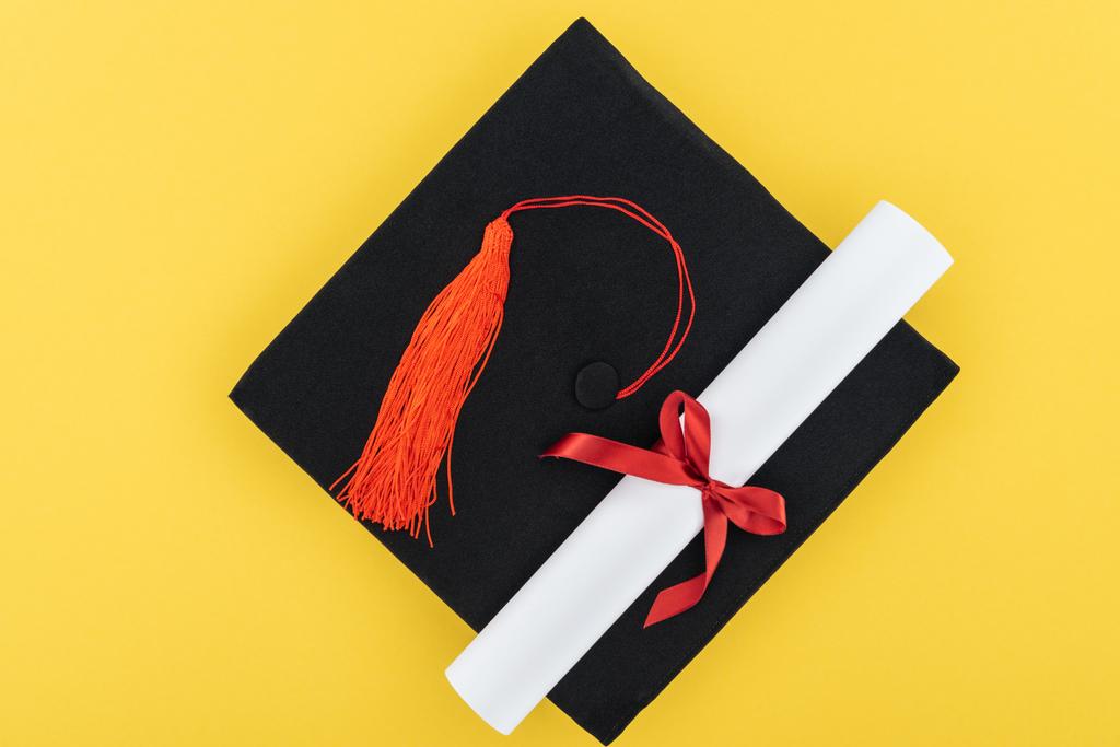 Ansicht von oben akademische Mütze und Diplom mit roter Schleife isoliert auf gelb - Foto, Bild