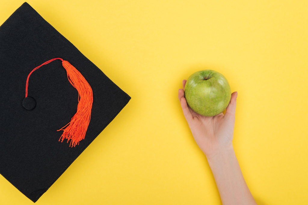 Przycięte widzenia kobieta z akademickiego Nakrywka zielone jabłko na powierzchni żółty - Zdjęcie, obraz