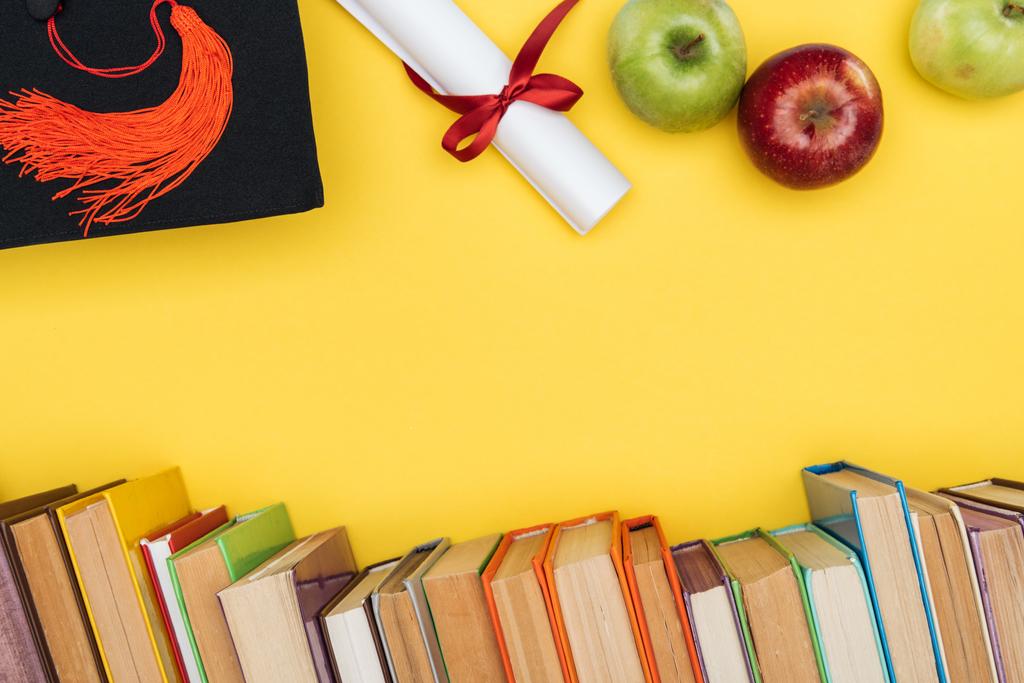 Vista superior de livros, maçãs, gorro acadêmico e diploma na superfície amarela
 - Foto, Imagem