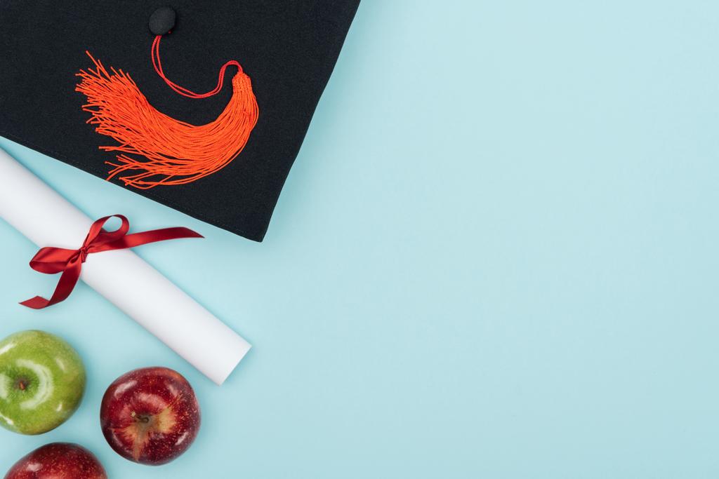 Top view of academic cap, diploma and apples on blue surface - Photo, Image