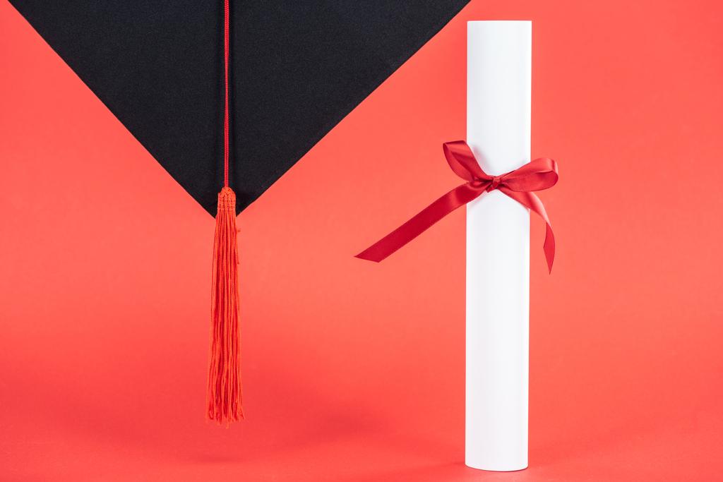 Academic cap with tassel and diploma with ribbon on red surface - Photo, Image