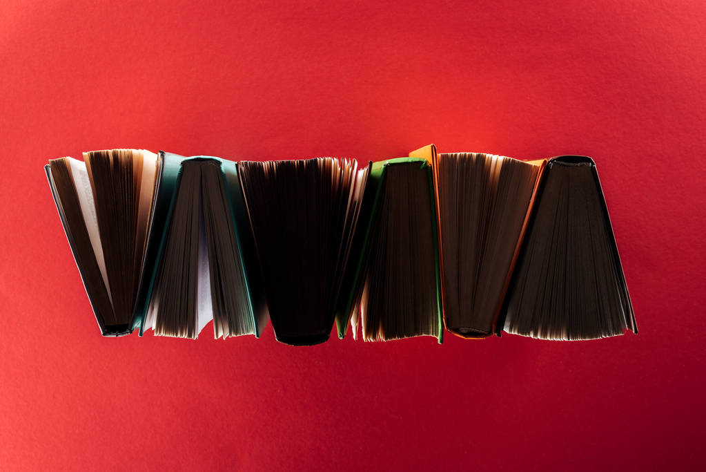 Вид сверху книг в твердой обложке на красной поверхности
 - Фото, изображение