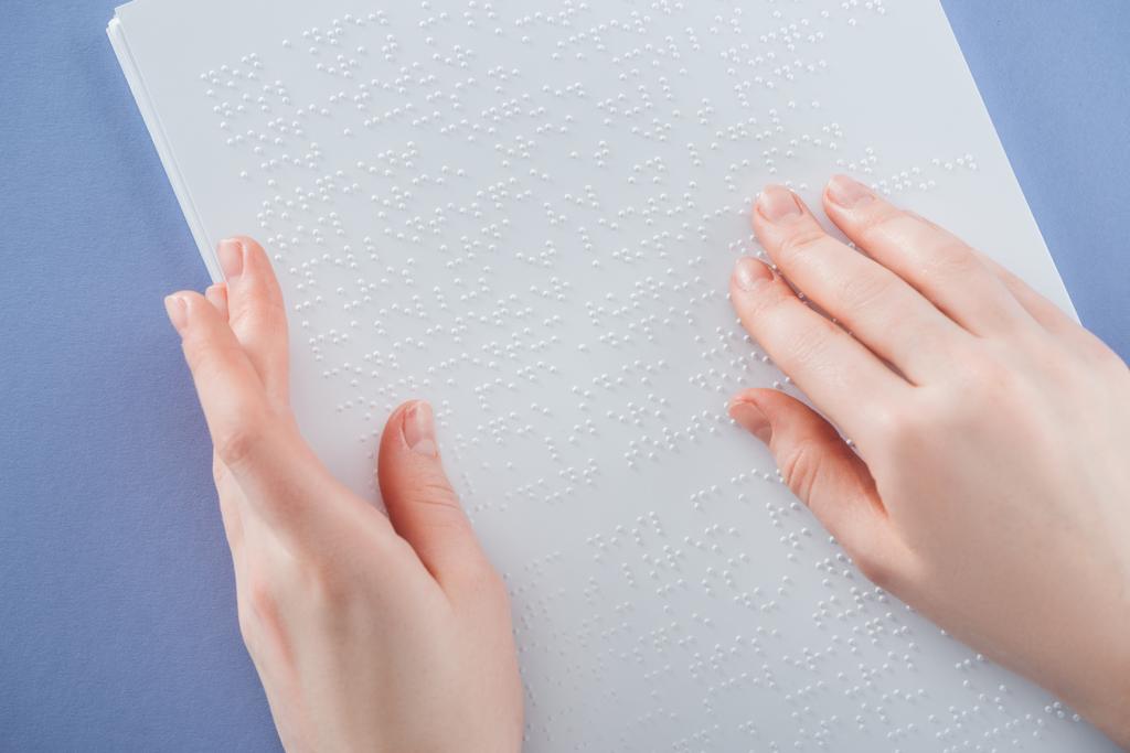 μερική άποψη της νεαρής γυναίκας ανάγνωσης braille κειμένου με το χέρι που απομονώνονται σε βιολετί - Φωτογραφία, εικόνα