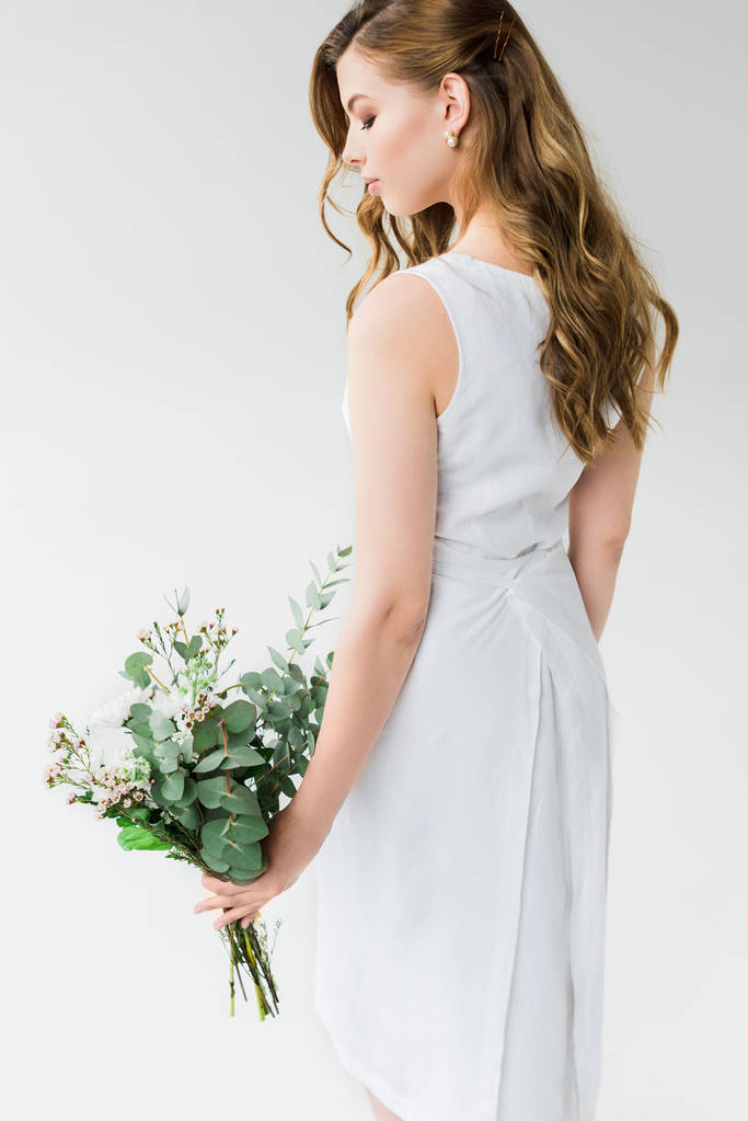 aantrekkelijke vrouw in elegante jurk kijken naar bloemen op wit - Foto, afbeelding