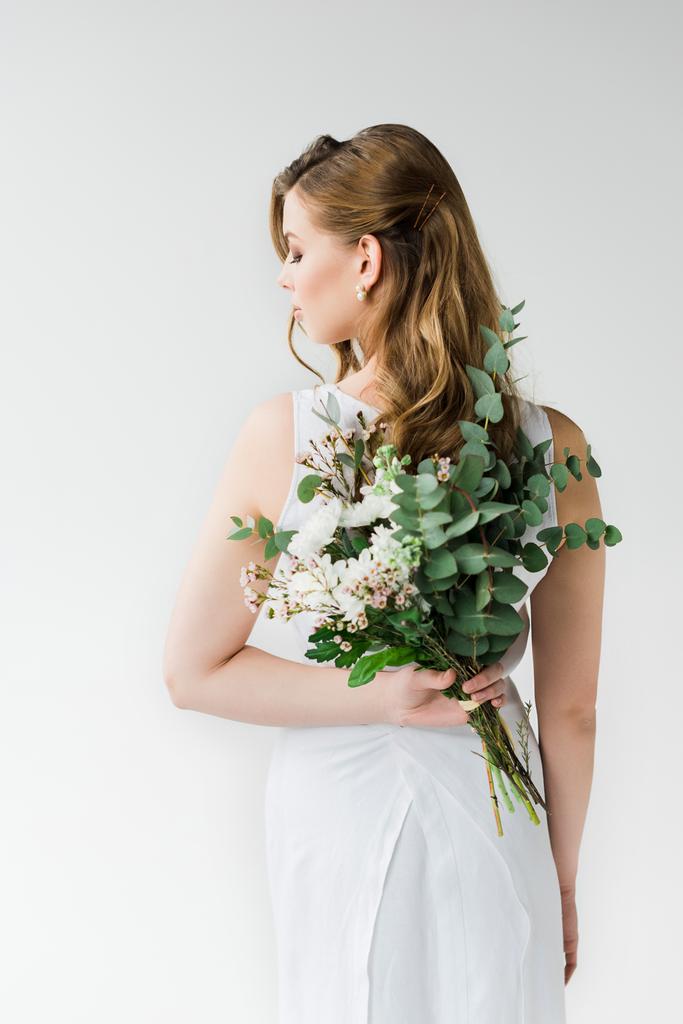 πίσω όψη της γυναίκας με κομψό φόρεμα κρατώντας λουλούδια πίσω από πίσω στο λευκό - Φωτογραφία, εικόνα
