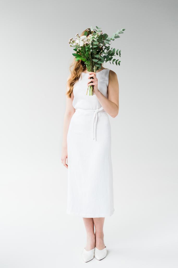 Frau im Kleid bedeckt Gesicht mit Blumen auf weißem Grund - Foto, Bild