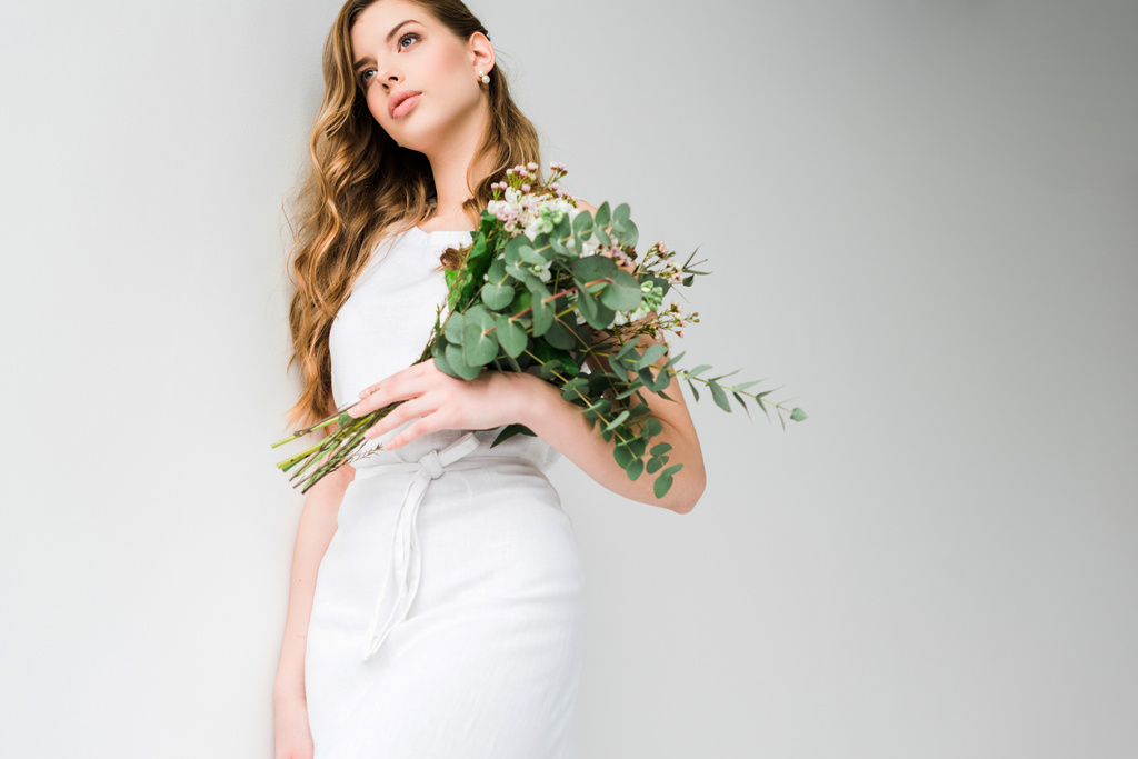 baixo ângulo vista da menina no vestido segurando buquê de camelacium e crisântemo flores com folhas de eucalipto no branco
  - Foto, Imagem