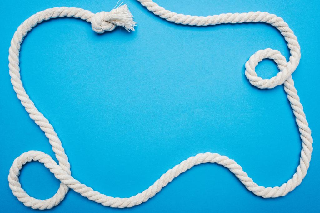 bovenaanzicht van wit zwaaide lang touw met knoop geïsoleerd op blauw - Foto, afbeelding