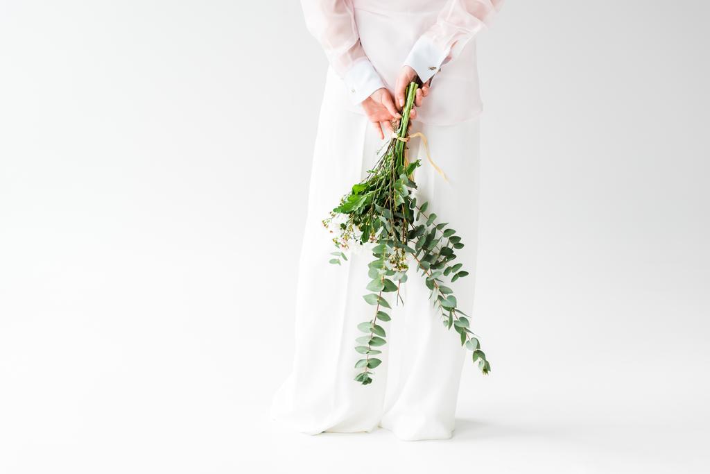 vue recadrée de la femme tenant bouquet de fleurs avec feuilles d'eucalyptus vert derrière le dos sur blanc
  - Photo, image