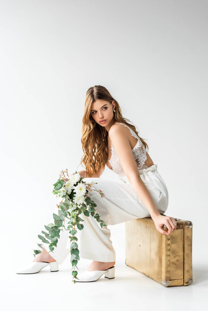jolie fille assise sur le sac de voyage et tenant bouquet avec des fleurs et des feuilles d'eucalyptus sur blanc
  - Photo, image