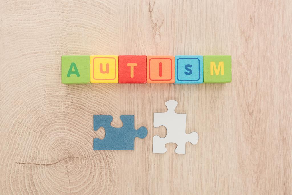 pohled shora autismu písma z různobarevné kostky poblíž díly skládačky na dřevěný stůl - Fotografie, Obrázek