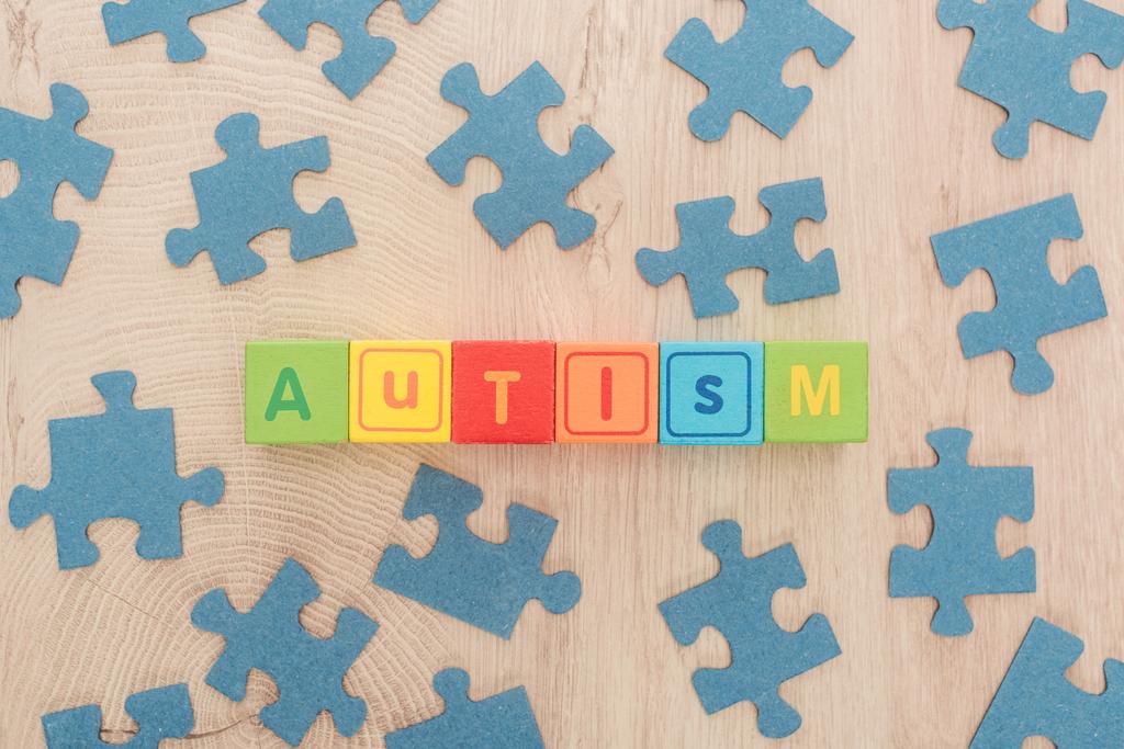 pohled shora autismu písma z různobarevné kostky mezi modré dílky na dřevěný stůl - Fotografie, Obrázek