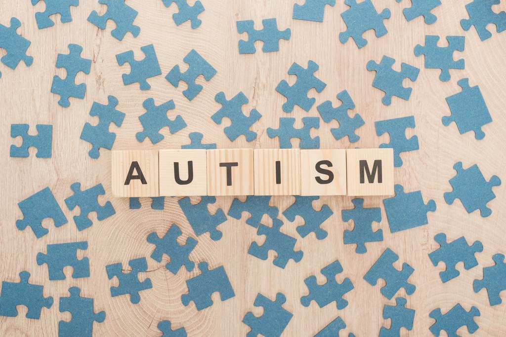 木製テーブルの上の青のパズル作品の中の木製のブロックで作られた自閉症のレタリングの平面図 - 写真・画像