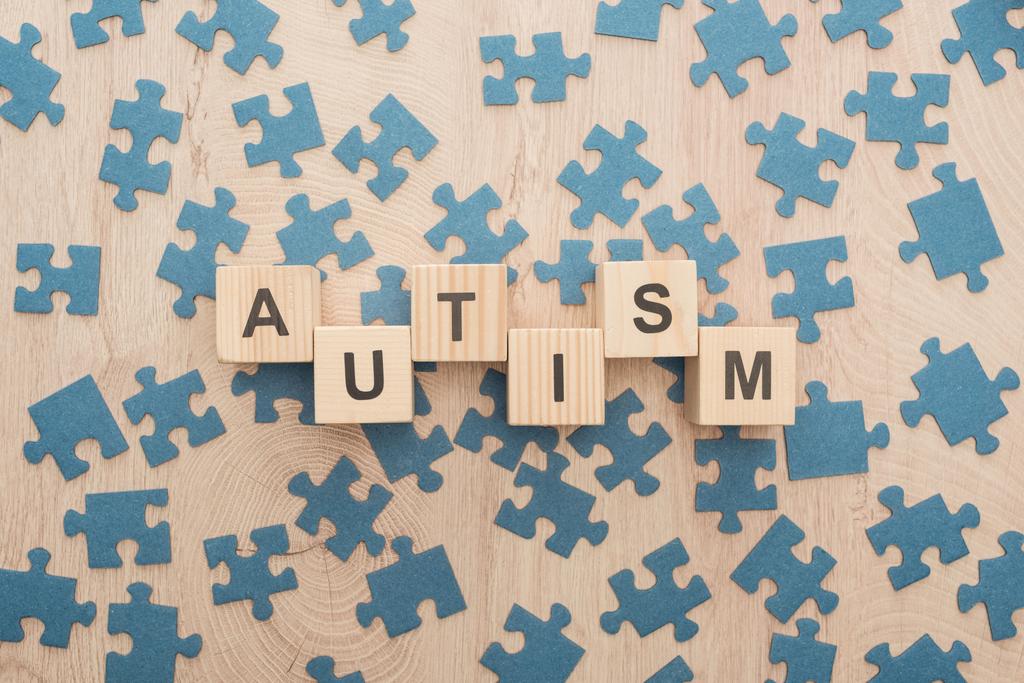Draufsicht auf Autismus-Schriftzug aus Holzklötzen zwischen Puzzleteilen auf Holztisch - Foto, Bild