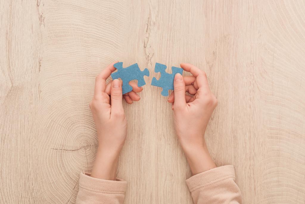 vista ritagliata di mani femminili che tengono puzzle blu sul tavolo di legno
 - Foto, immagini