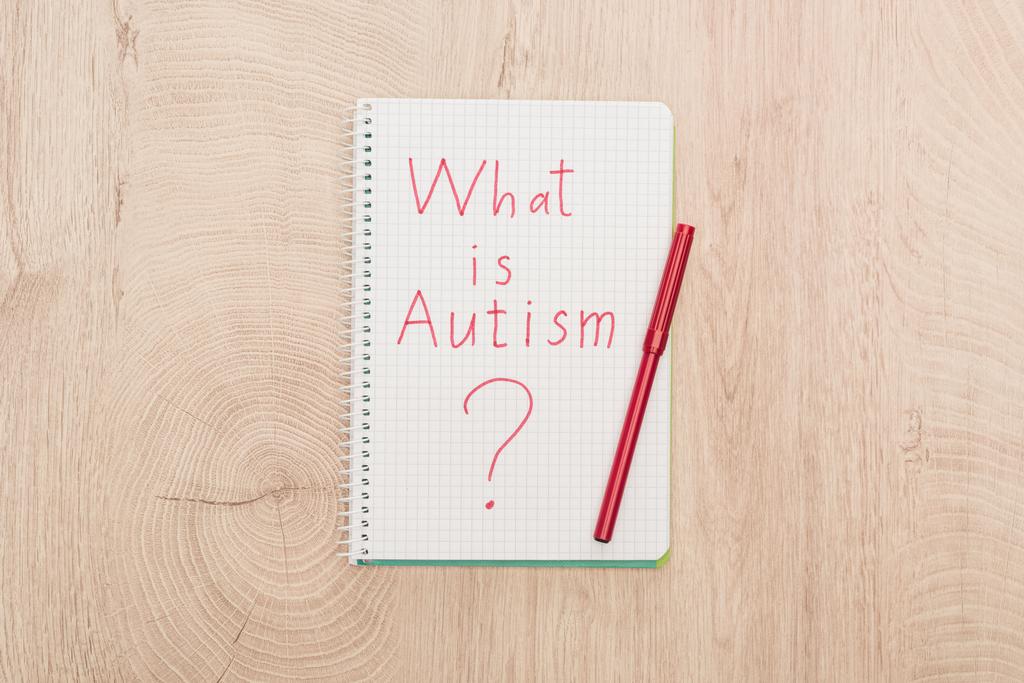 Draufsicht auf roten Filzstift und was ist Autismus-Frage in Notizbuch auf Holztisch geschrieben - Foto, Bild
