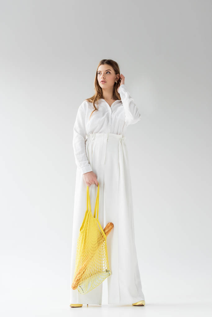 Młoda kobieta trzyma worek żółty ciąg z bagietki i butelkę mleka, stojąc na białym  - Zdjęcie, obraz