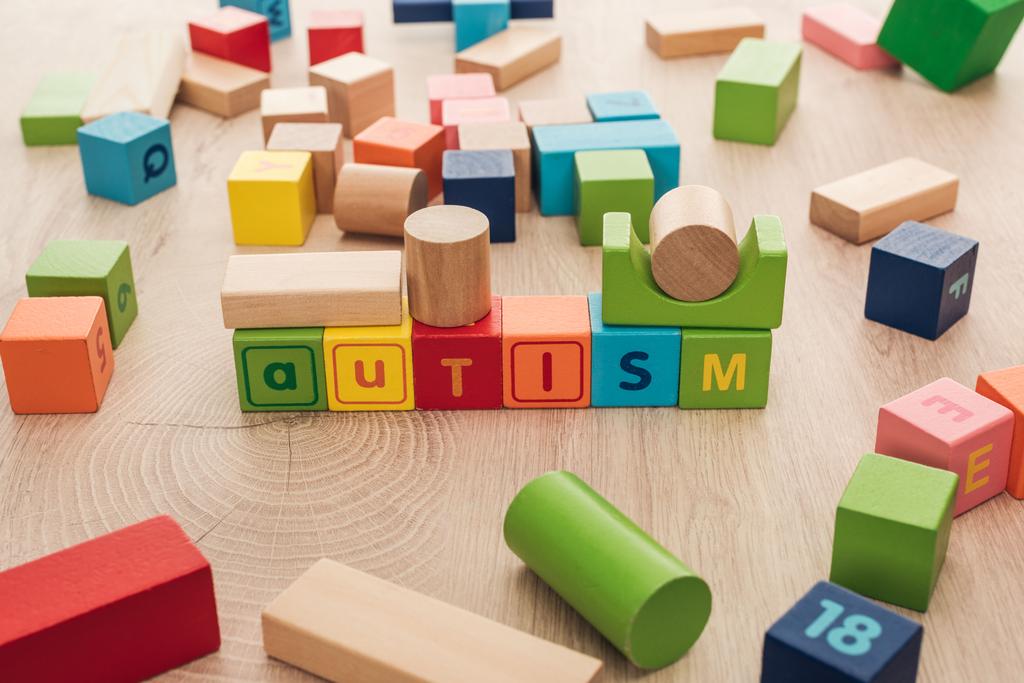 letras autistas hechas de cubos multicolores entre los bloques de construcción en la superficie de madera
 - Foto, imagen