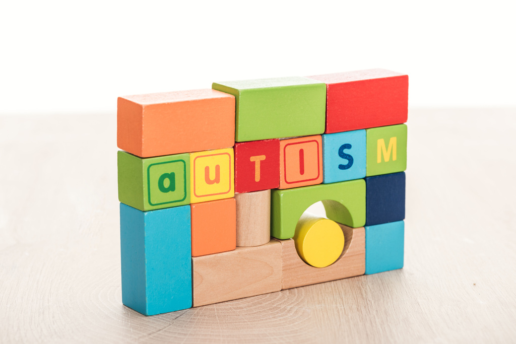autism lettering made of multicolored building blocks on wooden surface isolated on white - Photo, Image