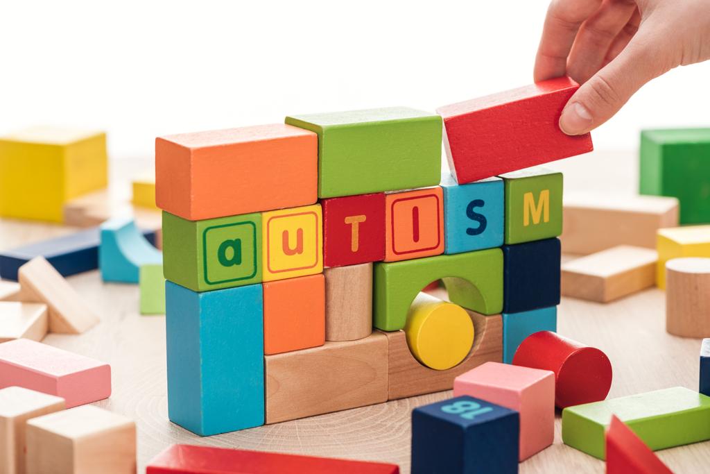 vista recortada de la mano femenina cerca de letras autistas hechas de bloques de construcción de colores en la superficie de madera aislada en blanco
 - Foto, Imagen