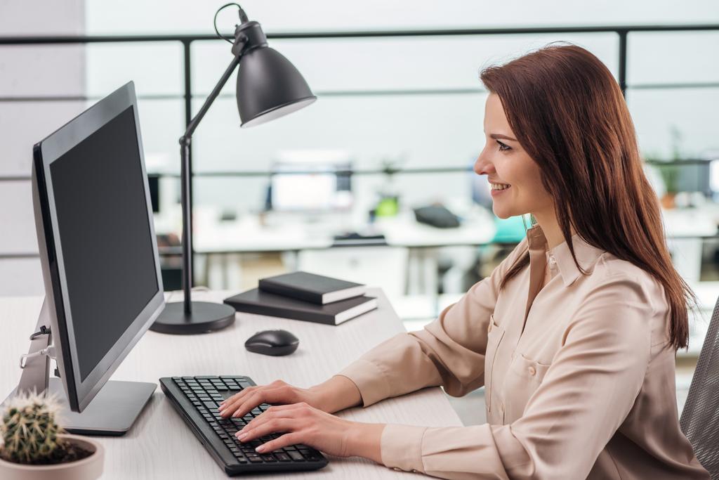 uśmiechający się młoda kobieta, wpisując na klawiaturze komputera w miejscu pracy w nowoczesnym biurze - Zdjęcie, obraz