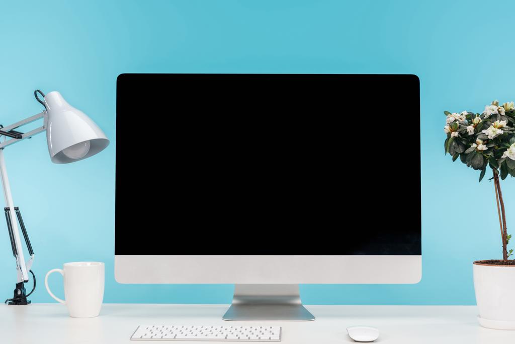 työpaikalla tietokone, lamppu, kuppi ja kukkaruukku valkoisella pöydällä sinisellä pohjalla
 - Valokuva, kuva