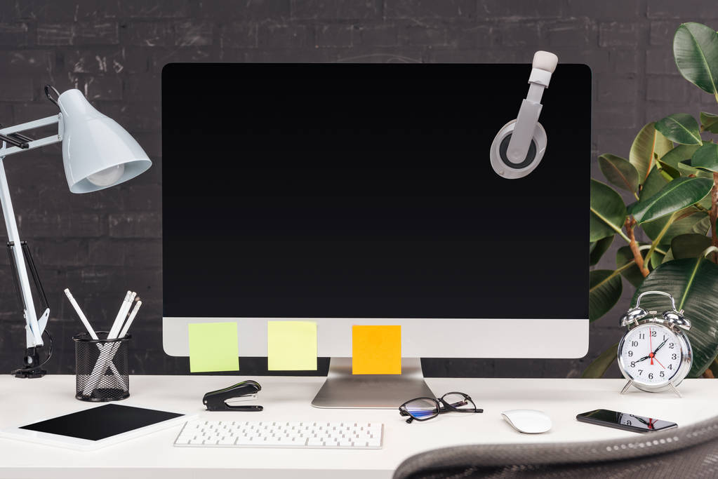 pracoviště se sluchátky a prázdné poznámky na monitoru počítače, lampu a šablon na bílém stole - Fotografie, Obrázek