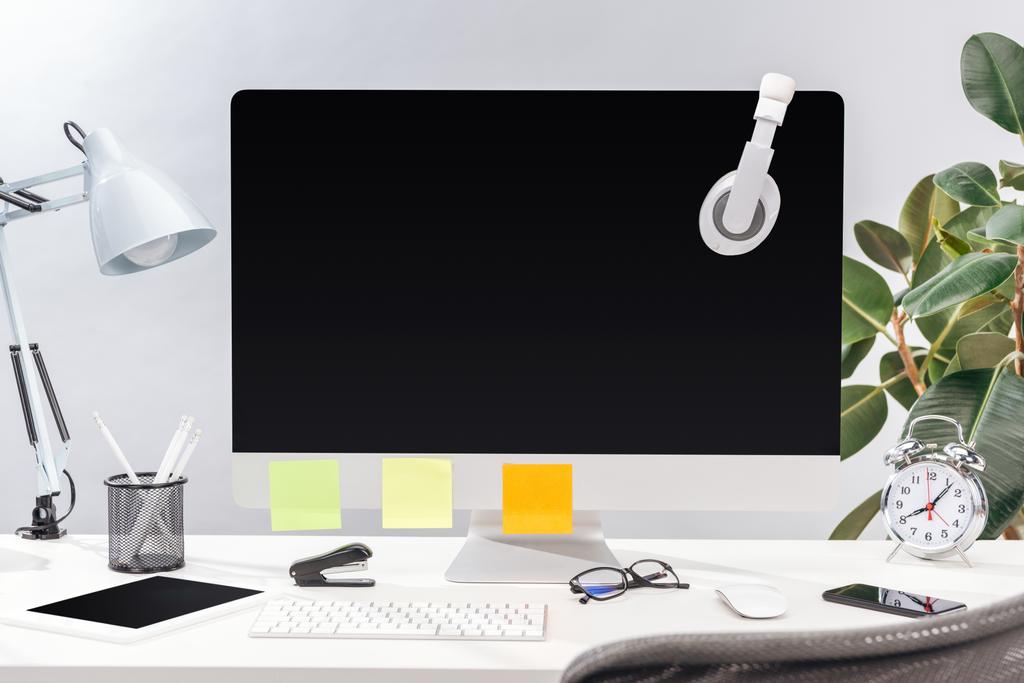 lugar de trabajo con auriculares y notas adhesivas vacías en el monitor de la computadora, lámpara y papelería en la mesa blanca sobre fondo gris
 - Foto, Imagen